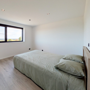 Chambre avec lit à parure verte, parquet clair et fenêtre offrant une vue dégagée.