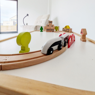 Circuit de train en bois avec petites maisons et personnages, jouet d'enfant posé sur une table.