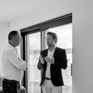 Deux hommes discutant devant une baie vitrée, photo en noir et blanc.