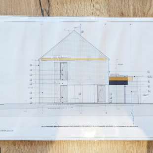 Plan d'architecte montrant l'élévation latérale gauche de la maison, posé sur une table en bois.