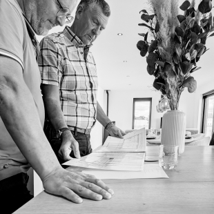 Visiteurs consultant des plans sur une table lors de la porte ouverte, photo en noir et blanc.